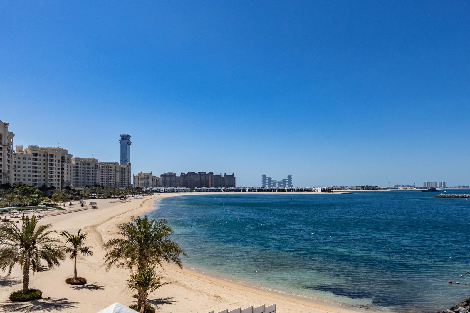 Breiter Dubai Strand mit Palmen, Meer und Skyline im Hintergrund