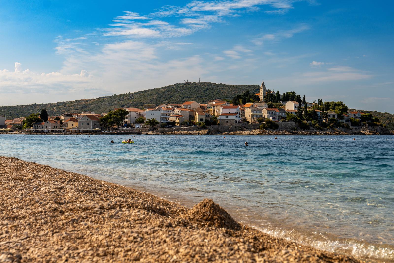 Kroatischer Kiesstrand mit Felsen, tiefblauem Meer und mediterraner Vegetation