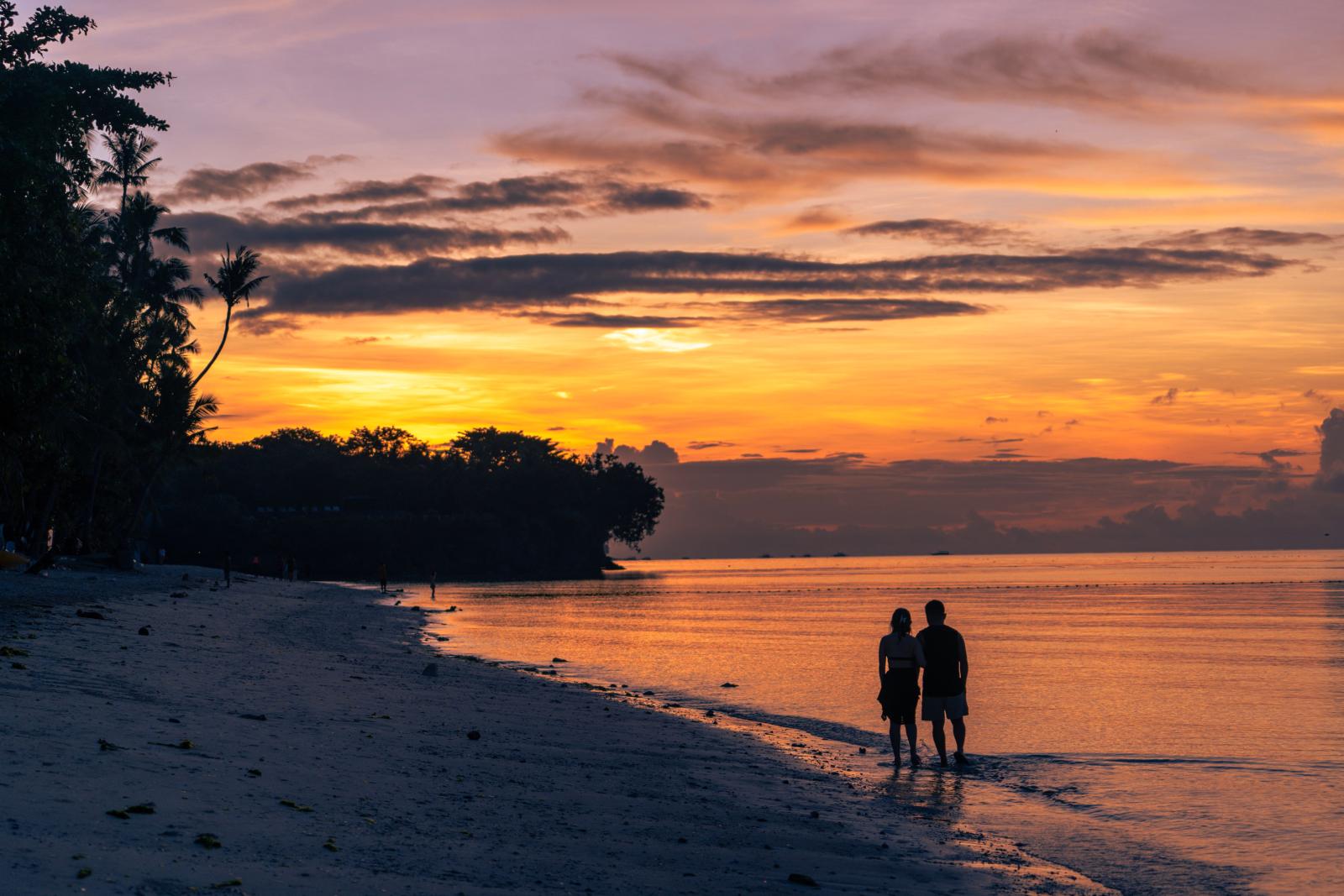 Paar am Strand bei Sonnenuntergang mit Blick auf das Meer und die tropische Inselkulisse