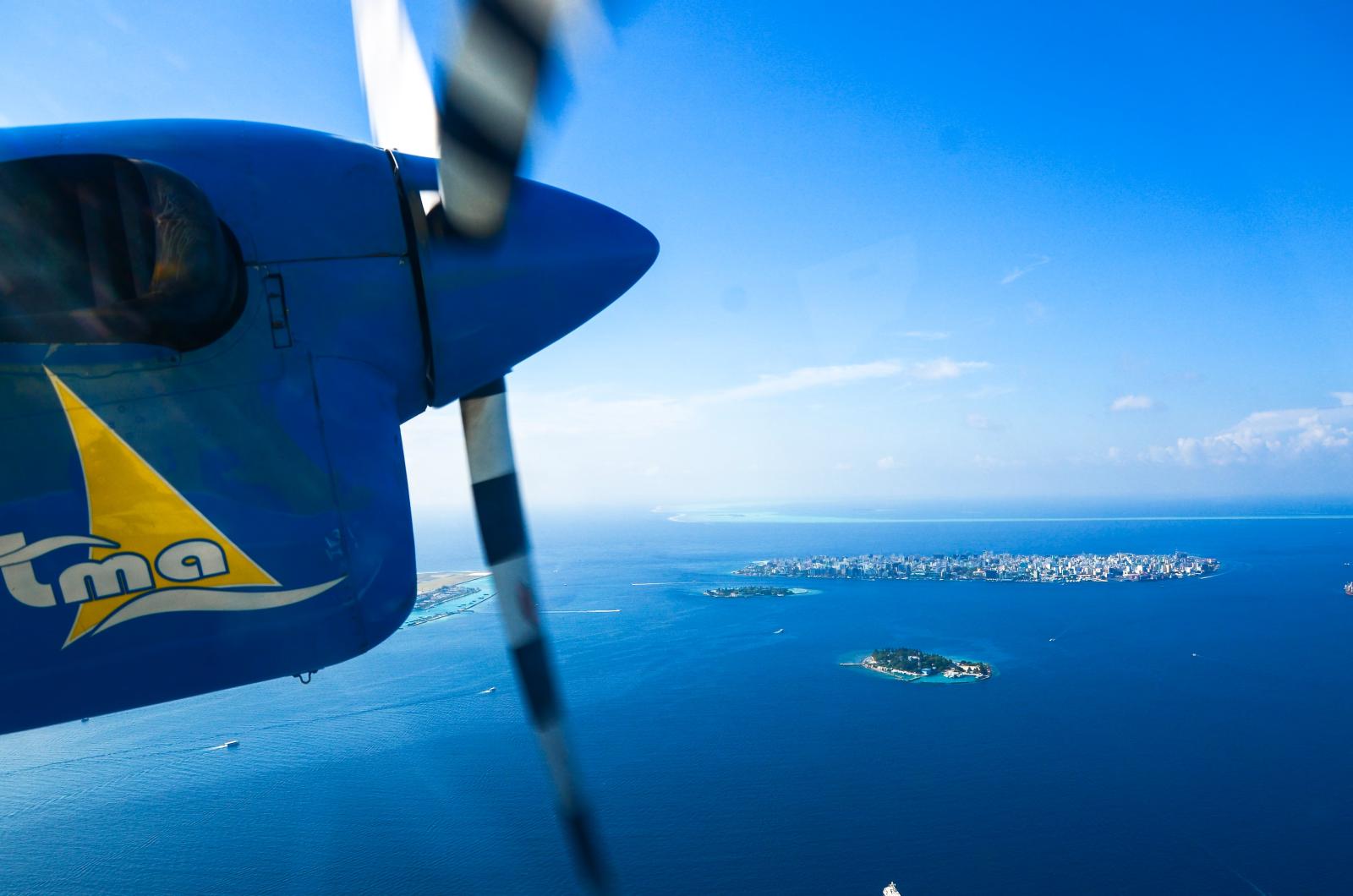 Wasserflugzeug über einer türkisfarbenen Lagune mit kleinen Inseln im Hintergrund