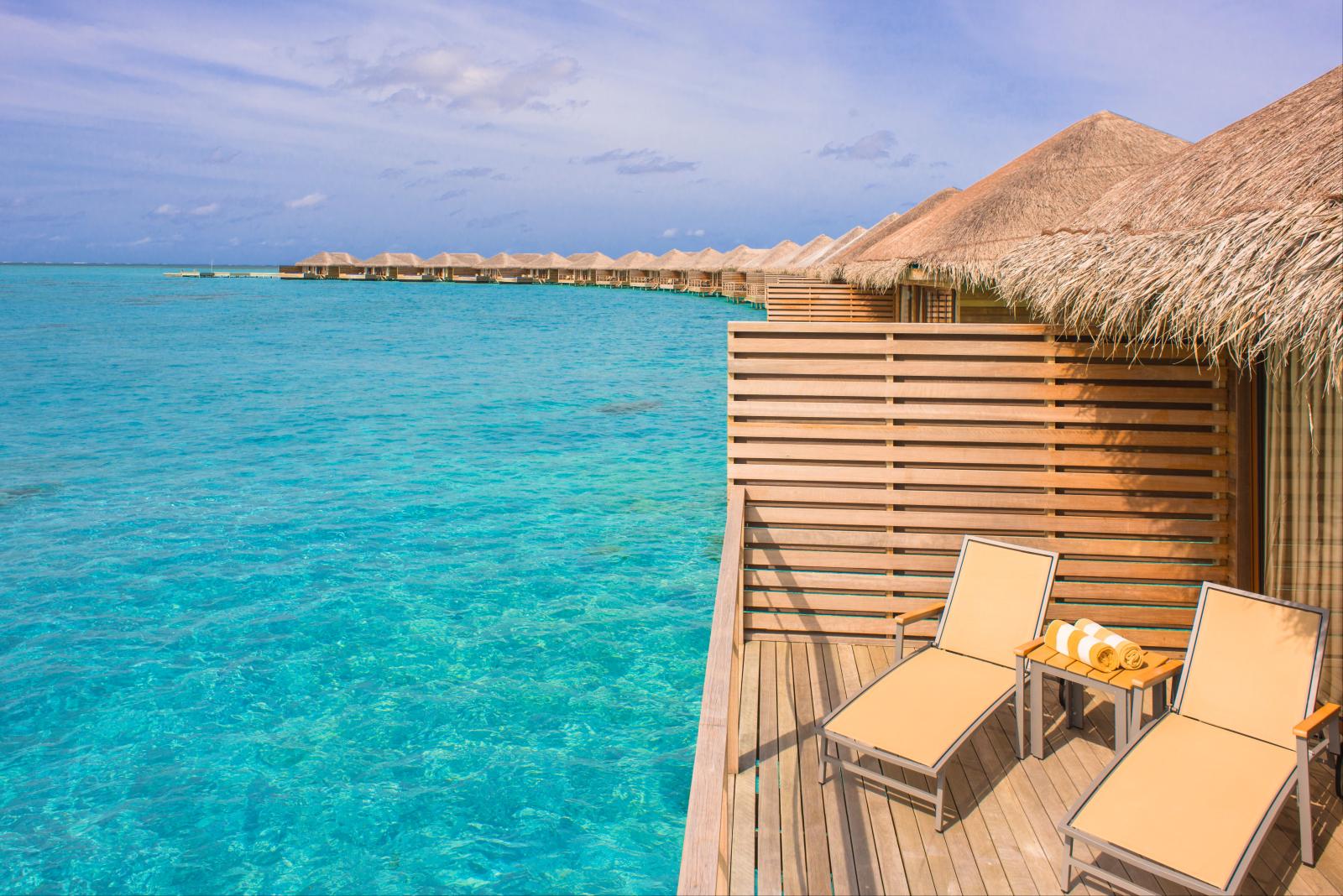 Terrasse eines Wasserbungalows mit Sonnenliegen und Blick auf die Lagune