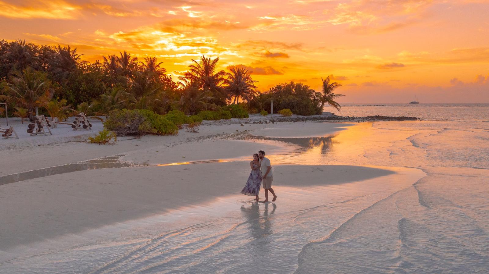 Paar am Strand bei Sonnenuntergang mit Palmen und Blick auf den Indischen Ozean