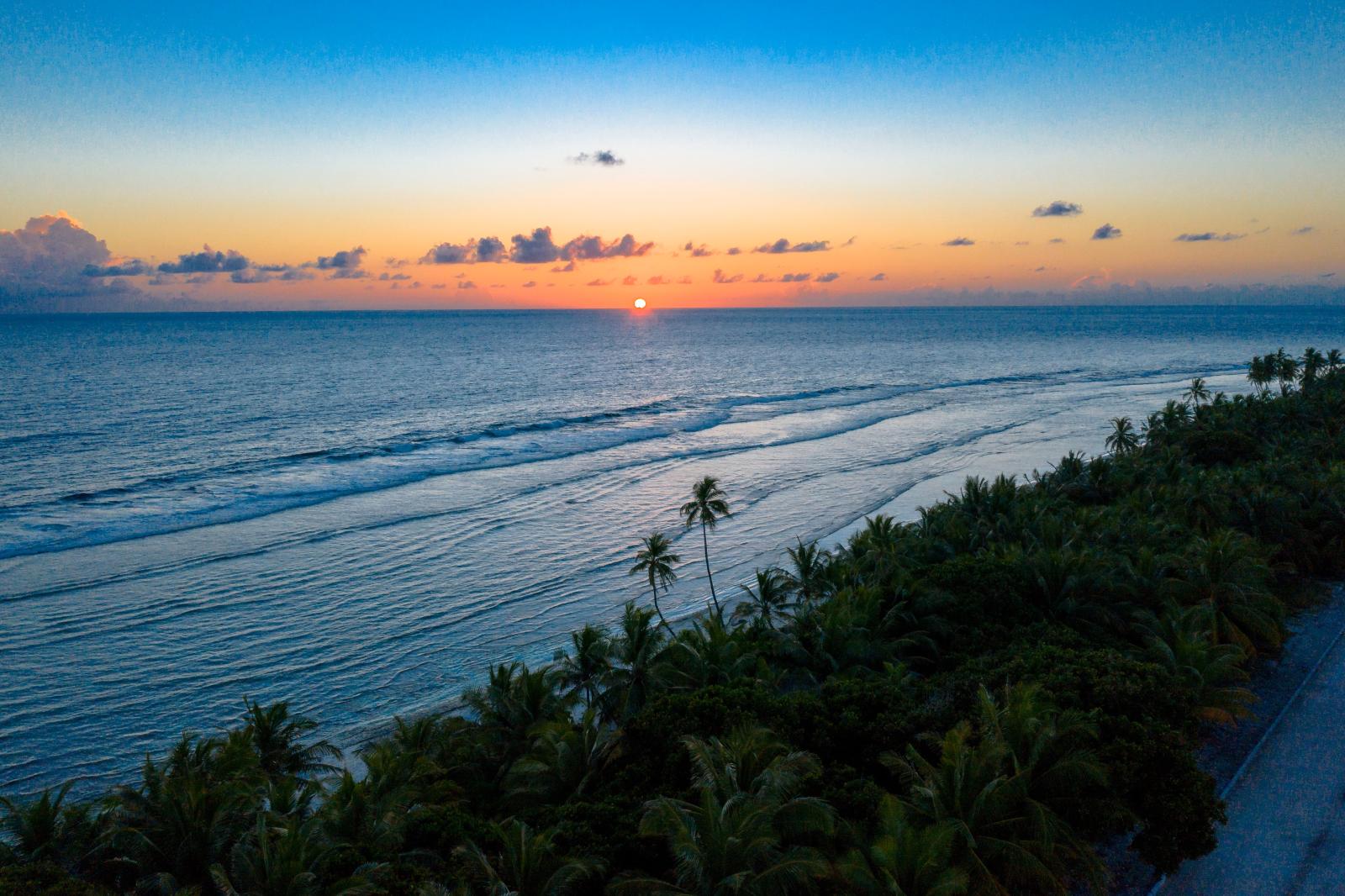 Sonnenuntergang über dem Indischen Ozean mit einer Malediveninsel im Vordergrund