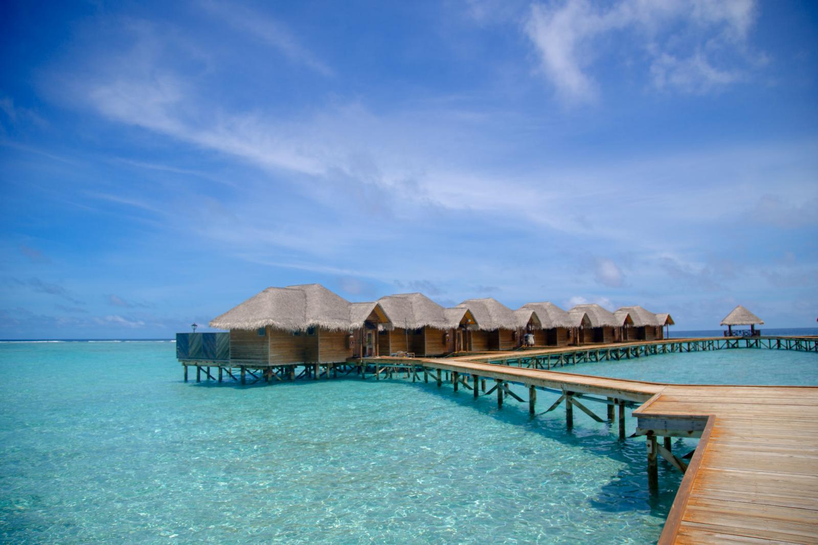 Wasserbungalows über einer türkisfarbenen Lagune mit tropischen Inseln im Hintergrund