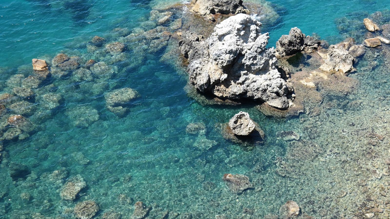 Beeindruckende Luftaufnahme einer felsigen Küste mit klarem türkisfarbenem Wasser und sichtbaren Felsformationen.