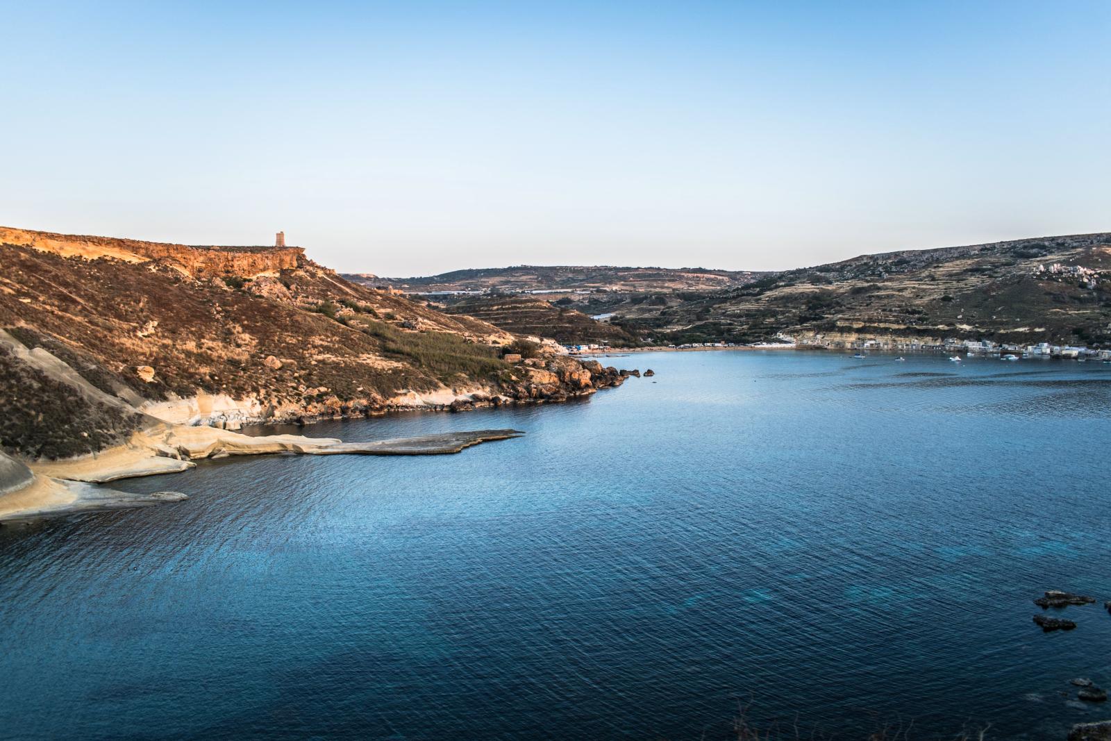 Eine ruhige Küstenszene mit ruhigem blauen Wasser und rauen Klippen im Hintergrund.