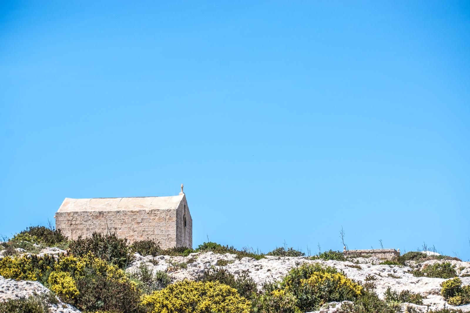 Eine rustikale Steinkapelle steht unter einem klaren blauen Himmel im ländlichen Malta.