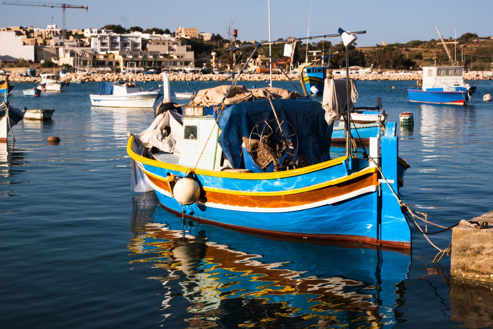 Traditionelles maltesisches Fischerboot vor einer Küstenkulisse]
