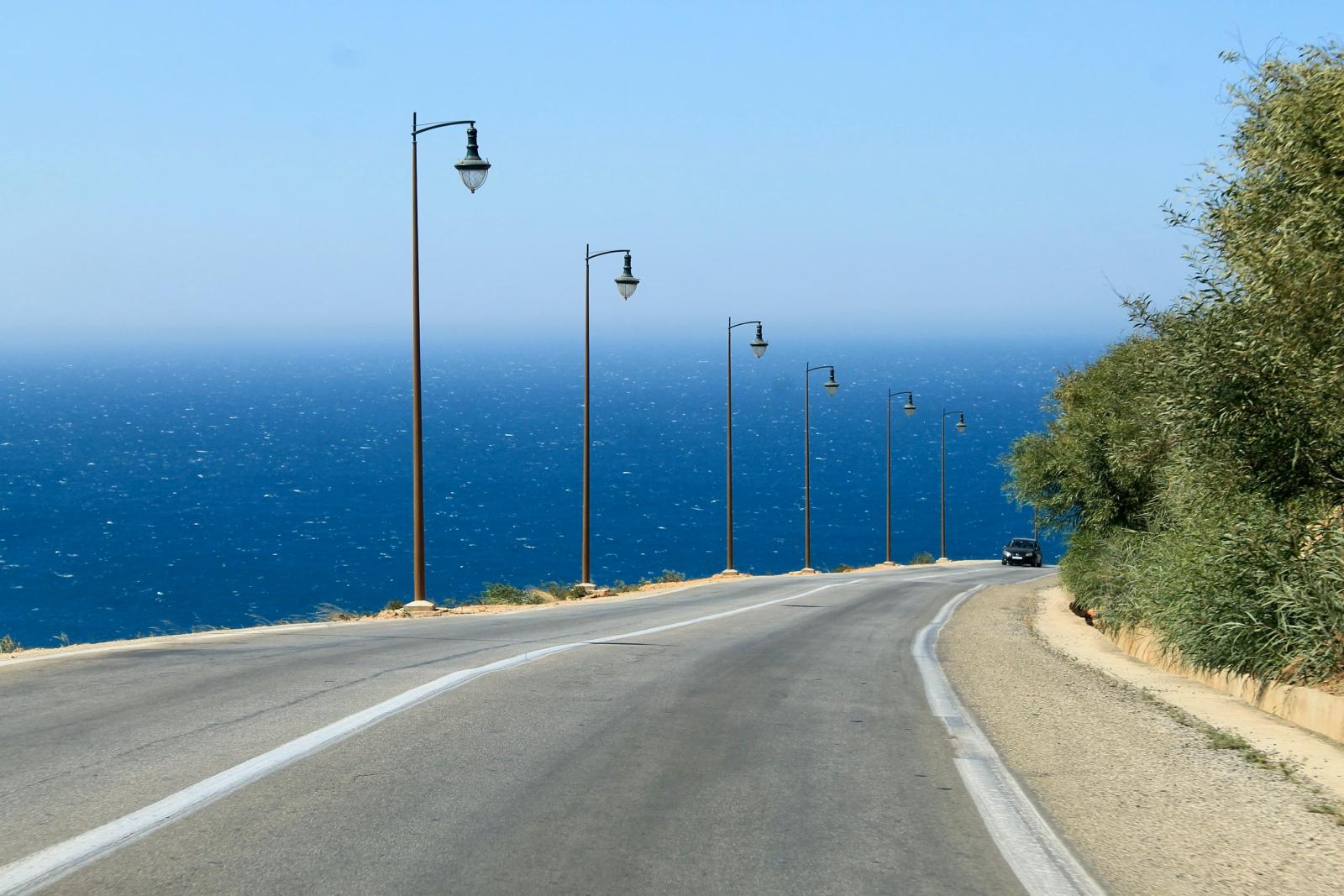 Szenische Küstenstraße mit Straßenlaternen am Rand, die den Blick auf den blauen Ozean freigibt.