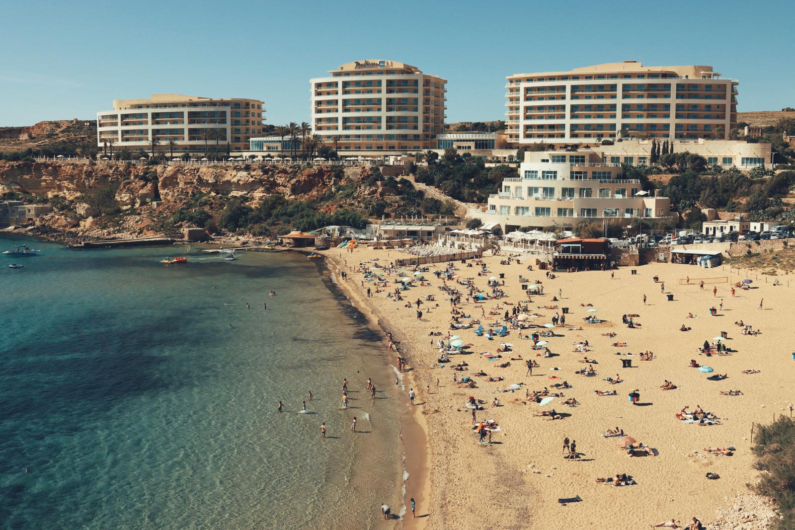 Eine lebendige Szene am sandigen Strand von Malta, wo Touristen die Sonne und das Mittelmeer genießen.