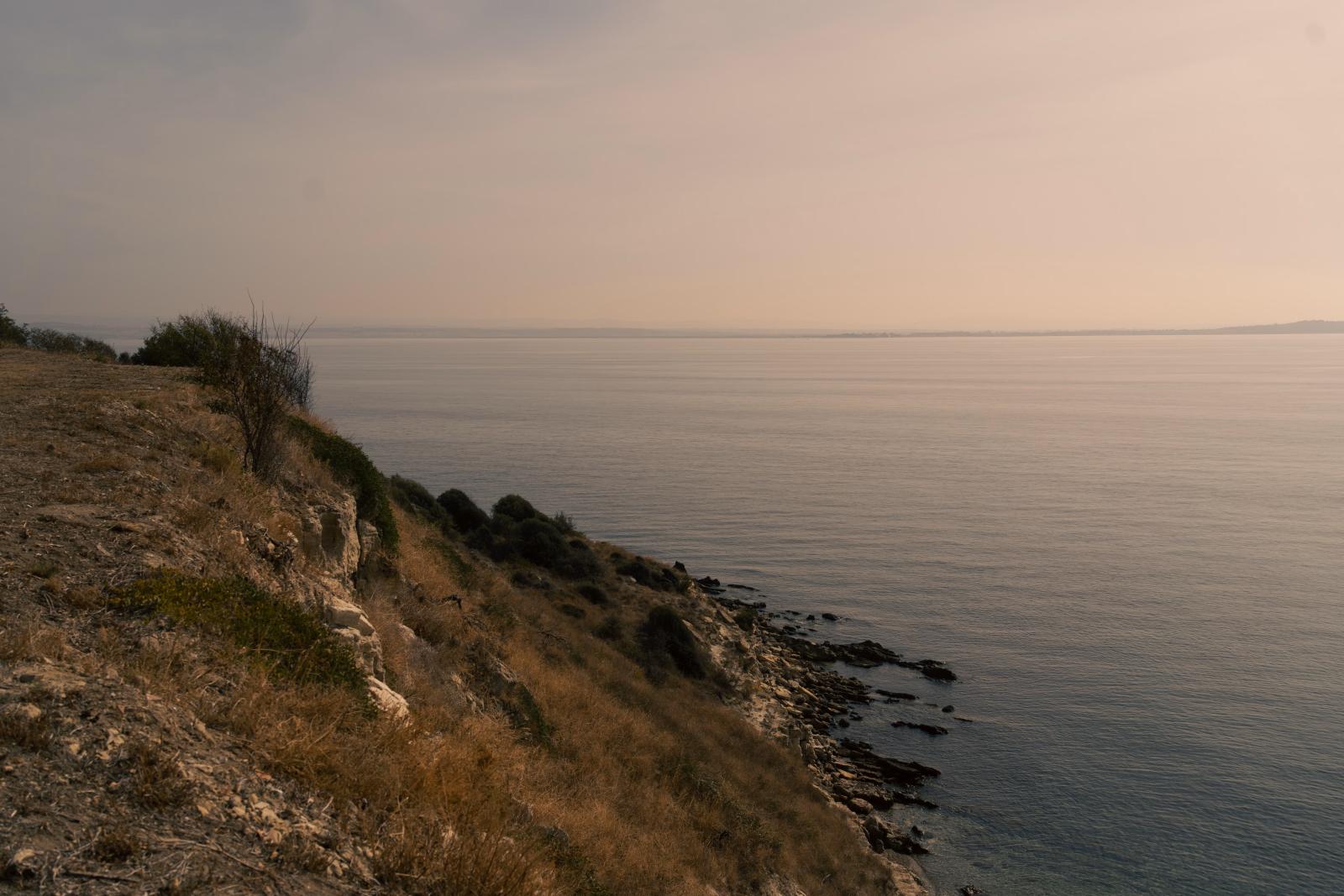 Eine ruhige Aussicht auf eine felsige Küste während der Morgendämmerung mit ruhigem Meer und sanfter Landschaft.