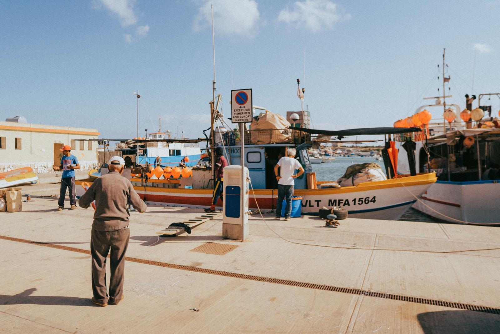 Fischer arbeiten im malerischen Hafen von Marsaxlokk, Malta, mit bunten Booten und klarem blauen Himmel.