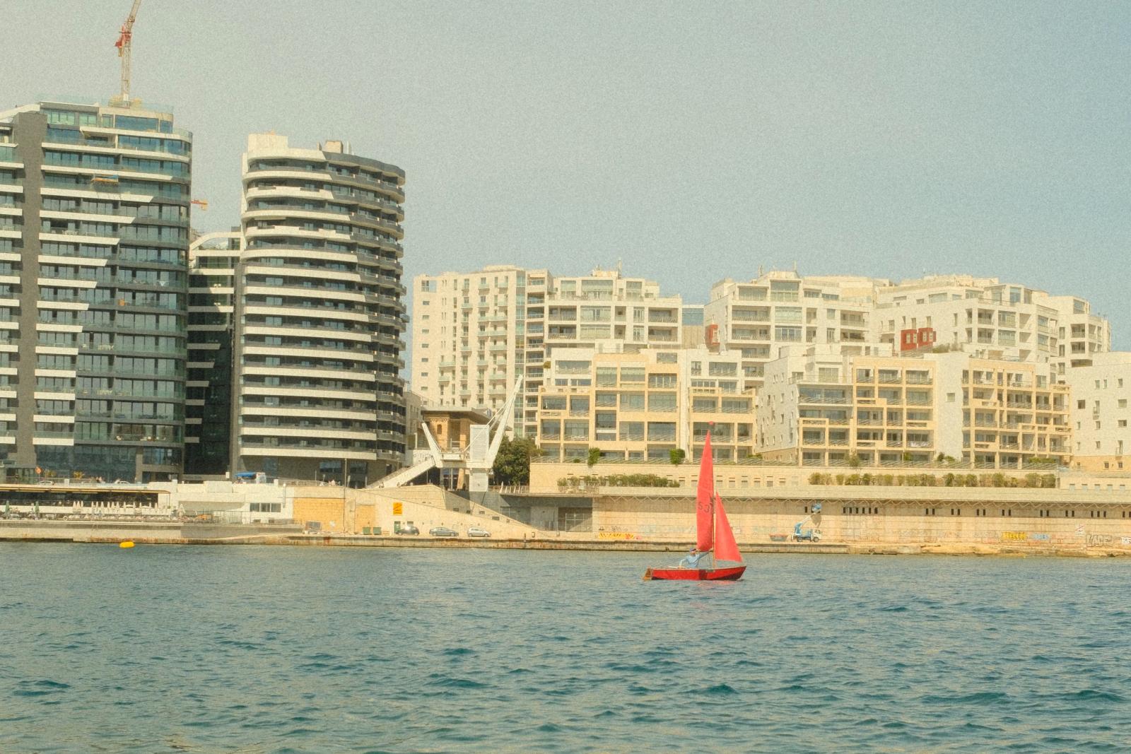  Blick über eine maltesische Bucht mit Hotelgebäuden und Mittelmeer im Hintergrund
