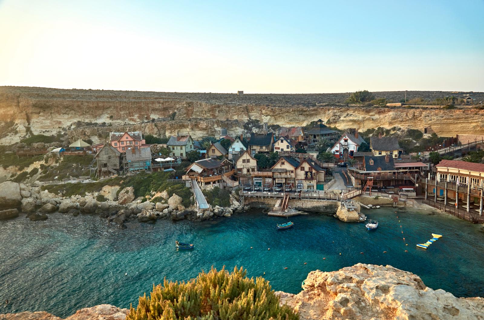 Eine atemberaubende Luftaufnahme des Popeye-Dorfs in Malta, eingebettet am Mittelmeer, das seinen einzigartigen Charme und natürliche Schönheit zeigt.