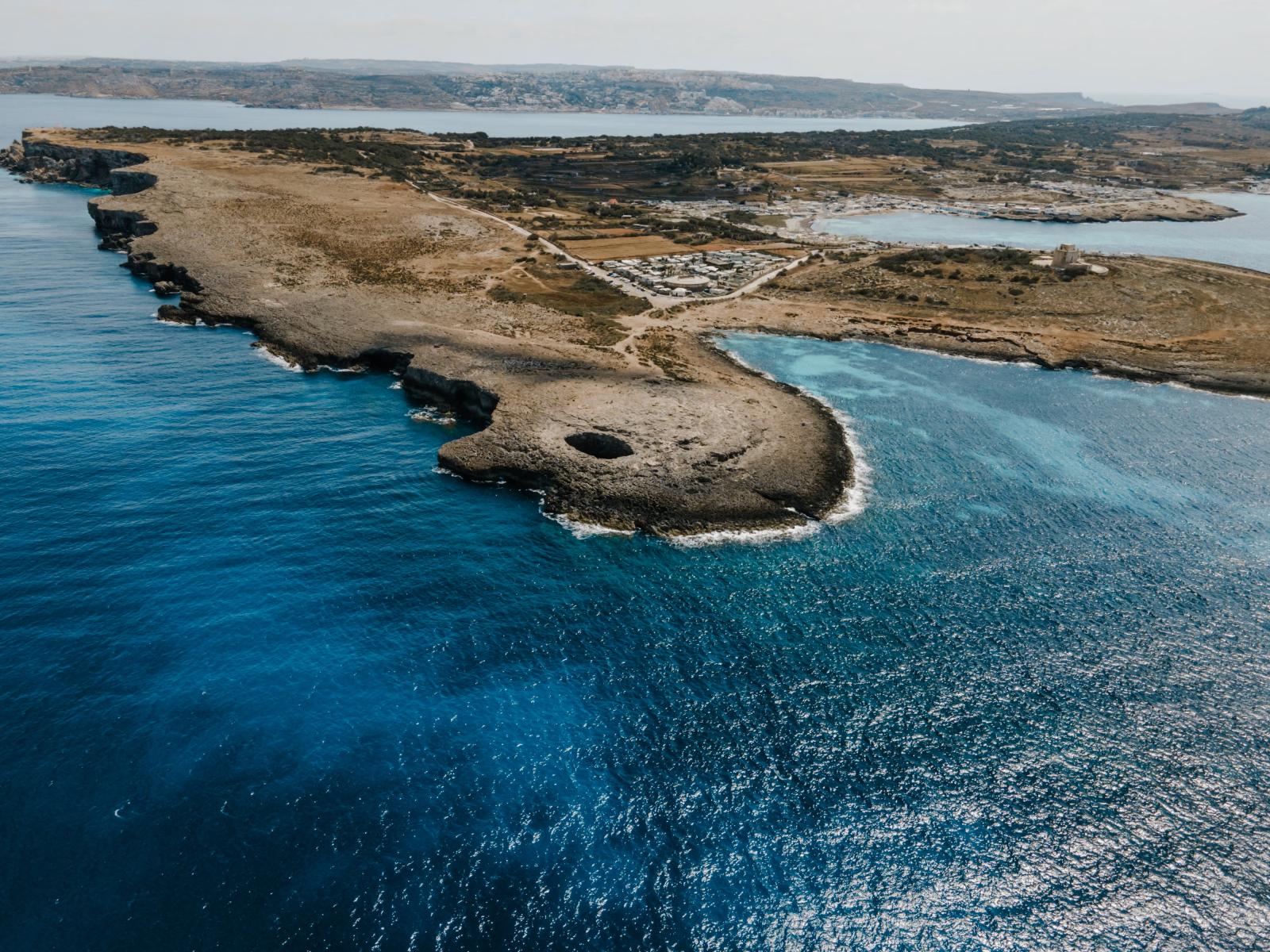 Eine atemberaubende Luftaufnahme der Küste von Il-Mellieħa in Malta, die türkisfarbenes Wasser und raues Gelände zeigt.