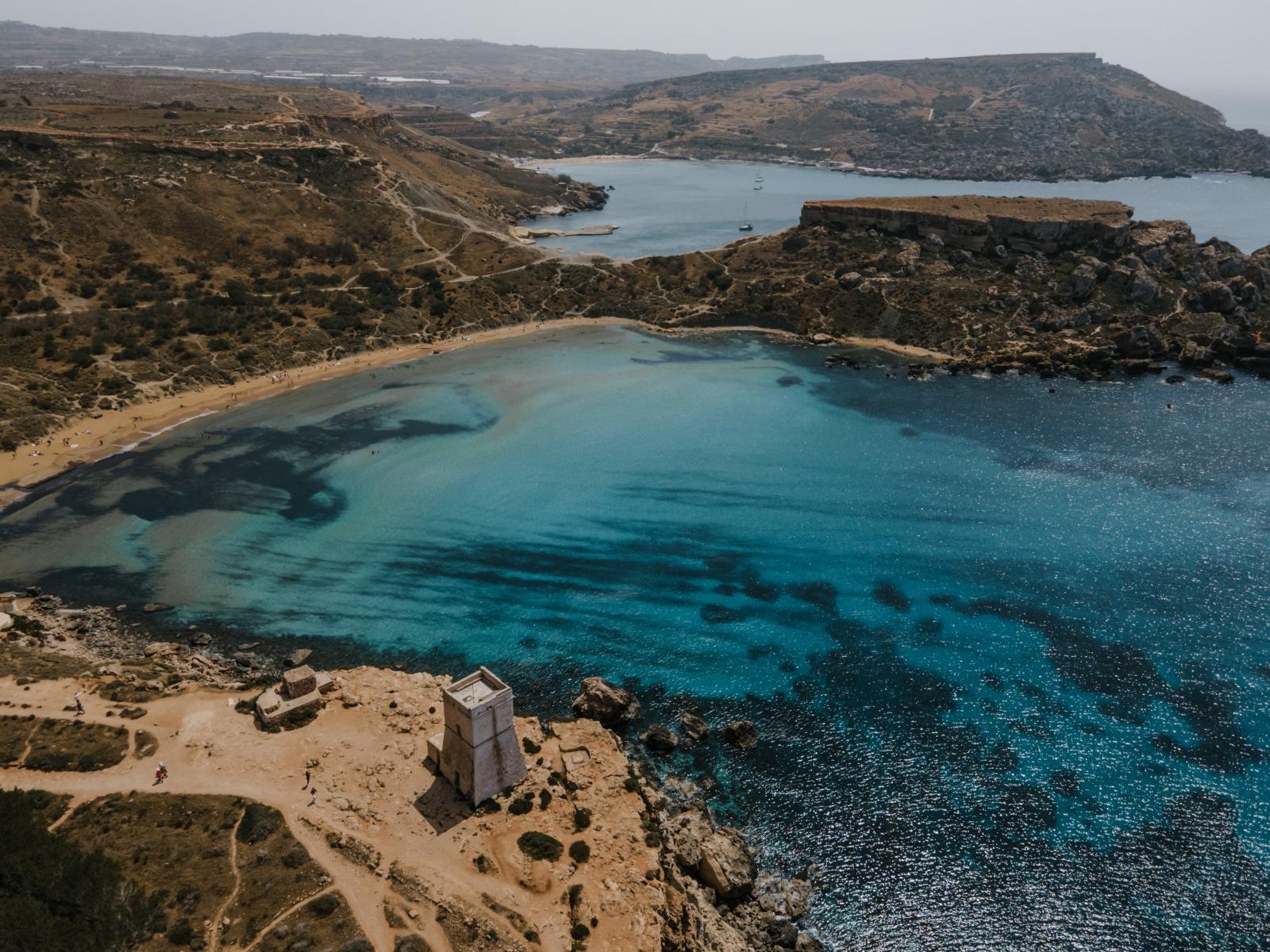 Sandstrand auf Malta mit klarem Wasser und sanft ansteigender Küste