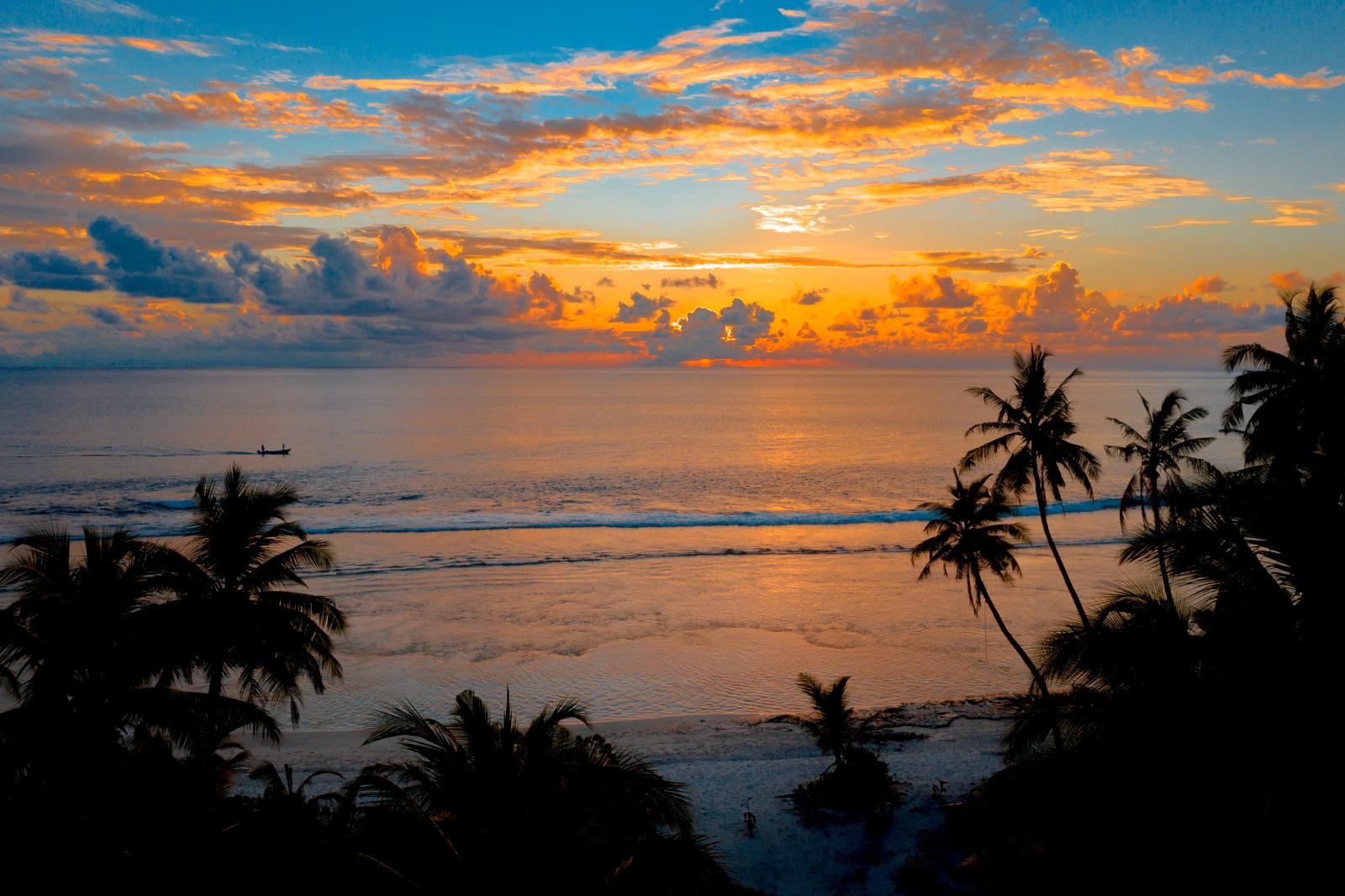Sonnenuntergang an einem Strand von Mauritius mit ruhiger Lagune und Palmensilhouetten.