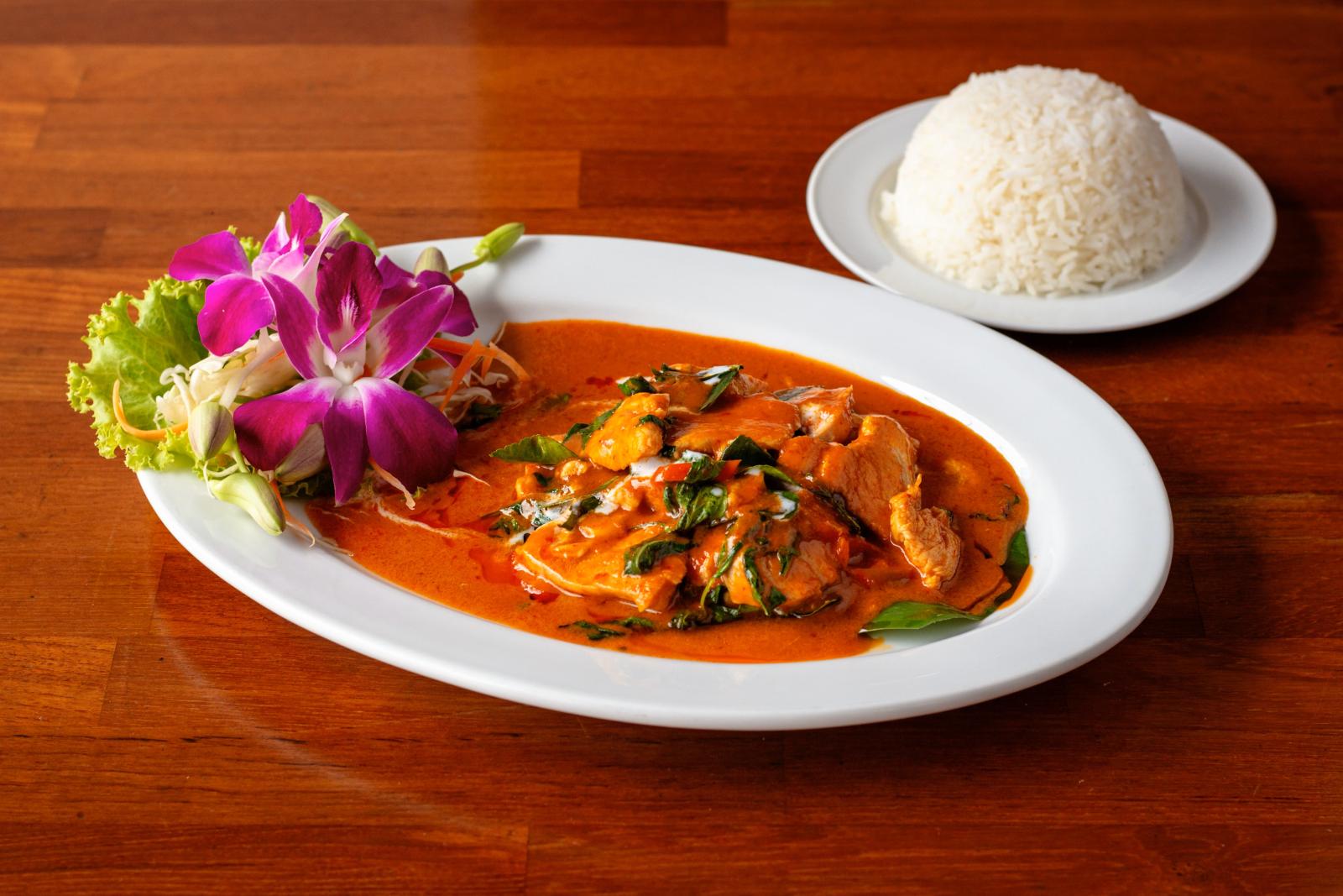 Leckeres thailändisches Curry mit lebhaften Aromen, serviert zusammen mit duftendem gedämpften Reis auf einem Holztisch.