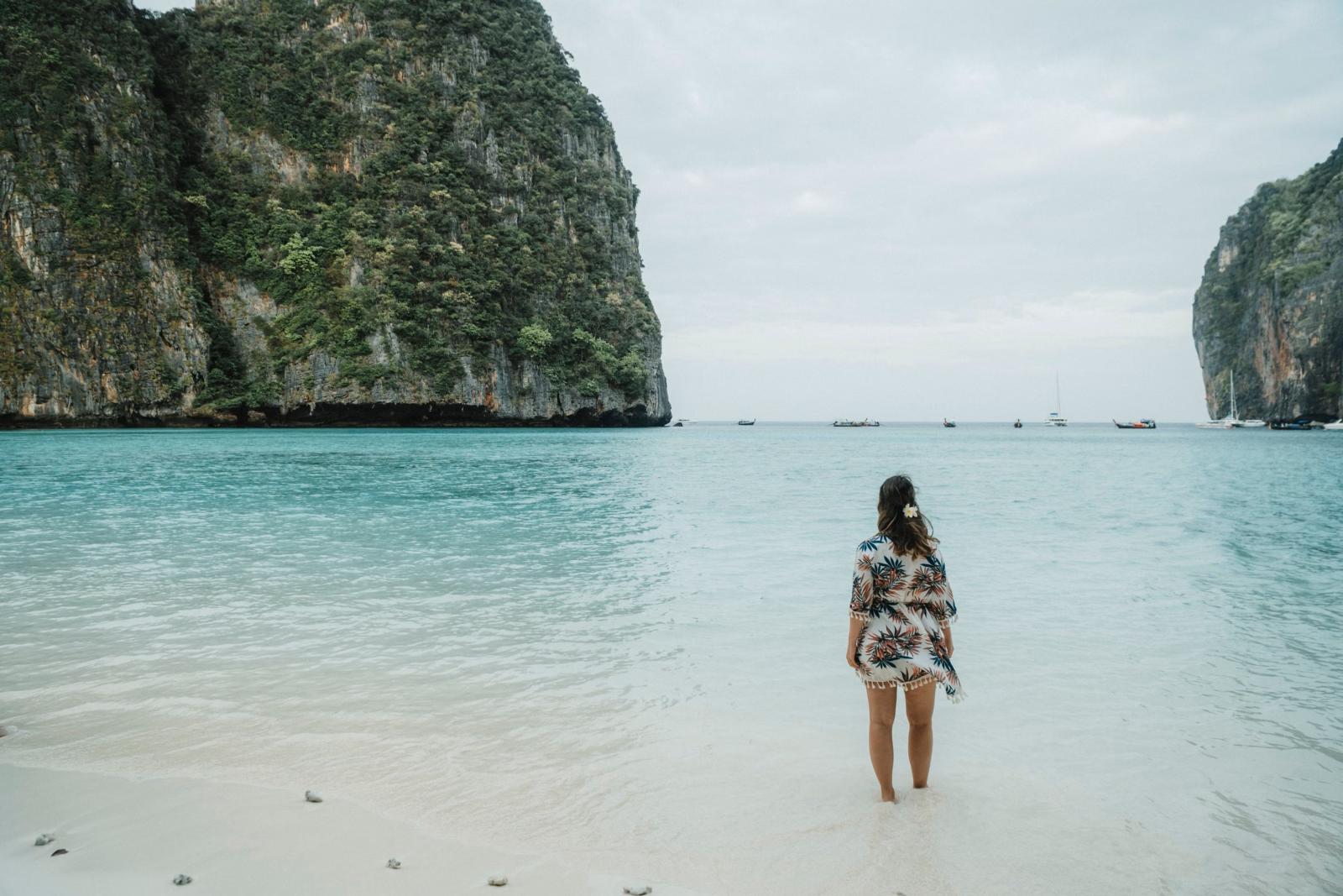 Eine Frau steht an einem malerischen Strand in der Maya Bay, Thailand, umgeben von türkisfarbenem Wasser und üppigen Klippen.