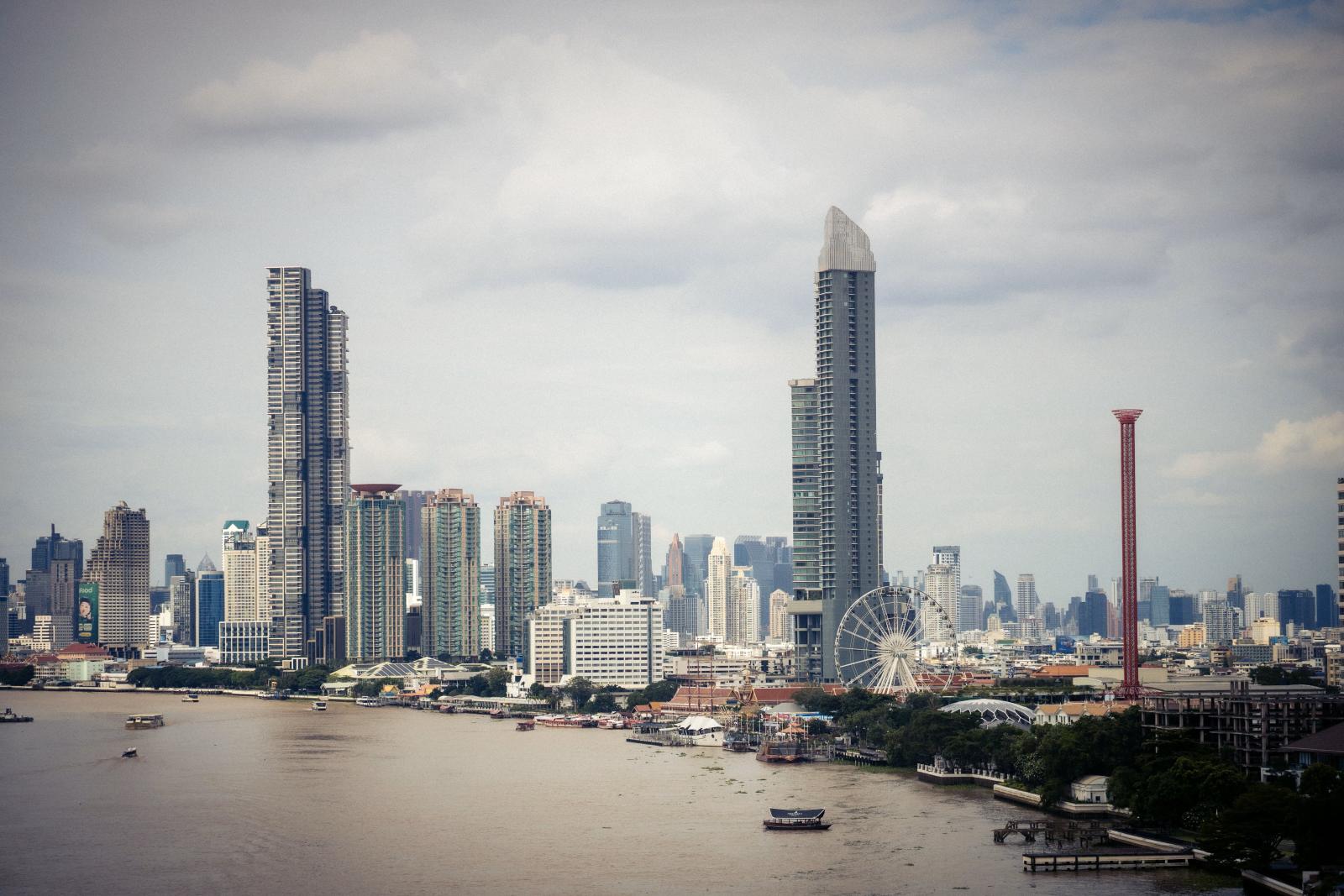 Blick auf die Skyline von Bangkok mit dem ikonischen Riesenrad und dem Chao Phraya Fluss bei Tag.