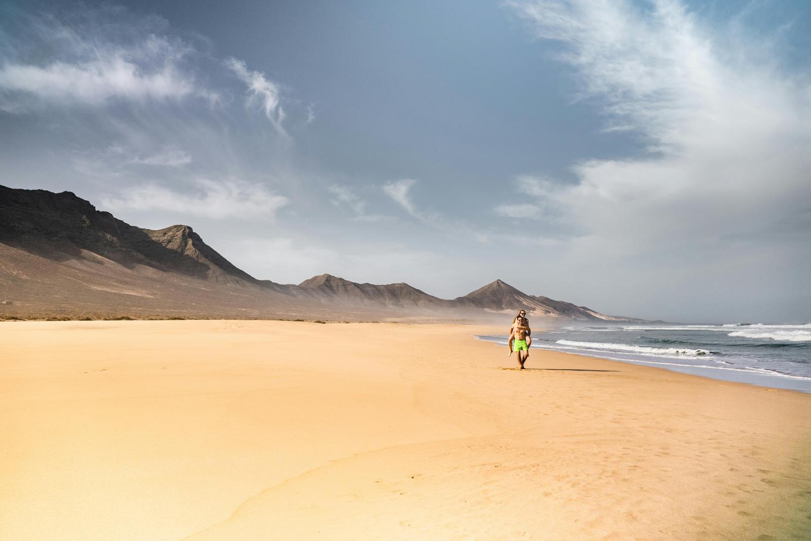Langer Sandstrand auf Fuerteventura mit Bergen und Meer