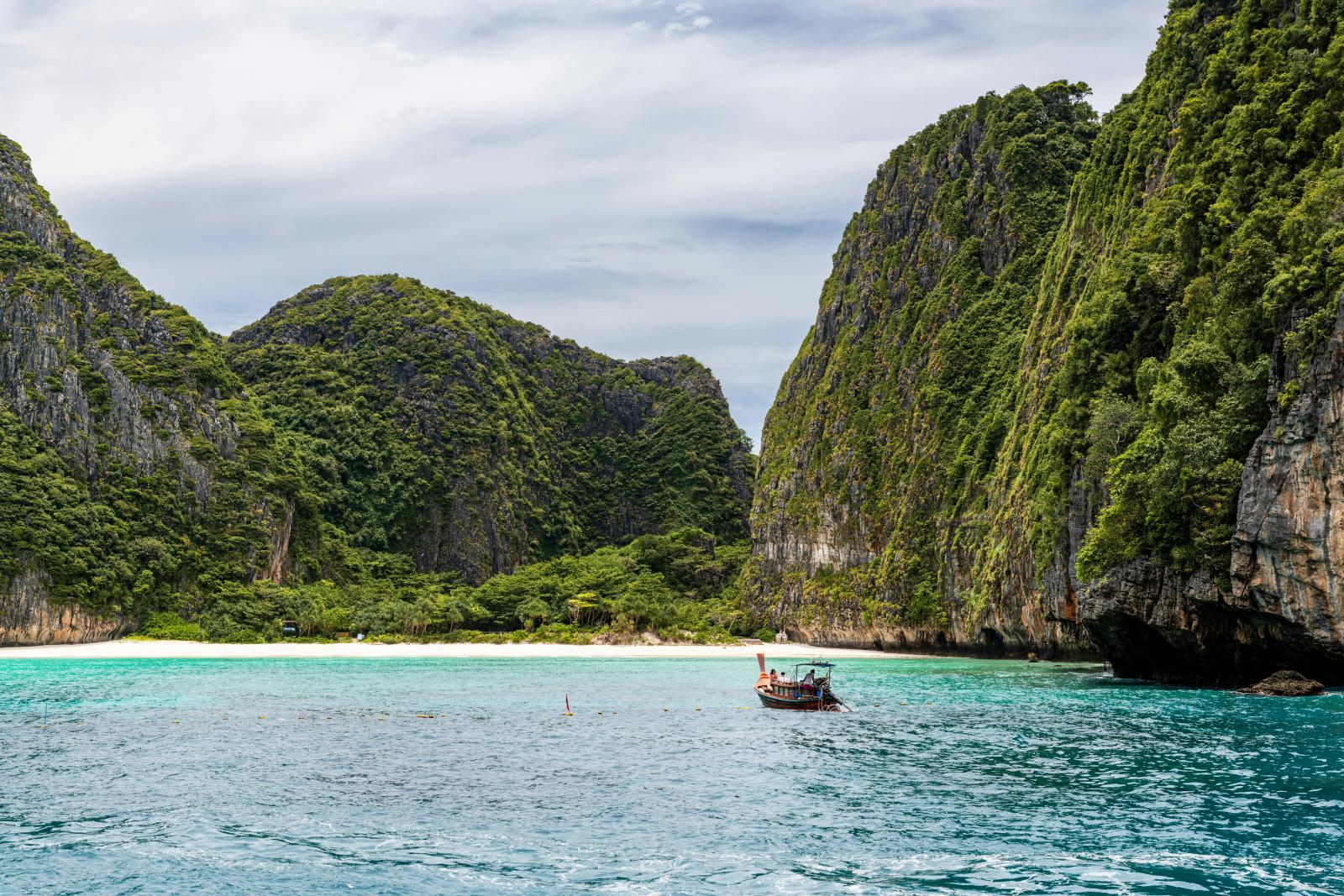 Thailand Urlaub Felsenbucht mit Longtailboot und türkisblauem Meer