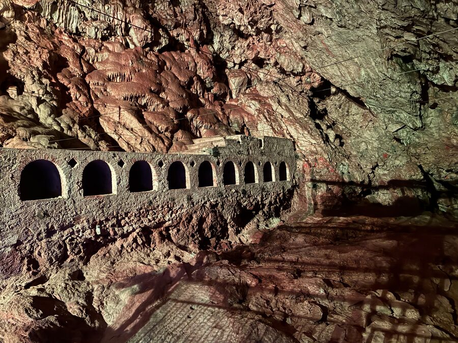 Das Innere der Grotte du Lazaret in Nizza mit rotbraunem Fels und einer Mauer mit Bögen