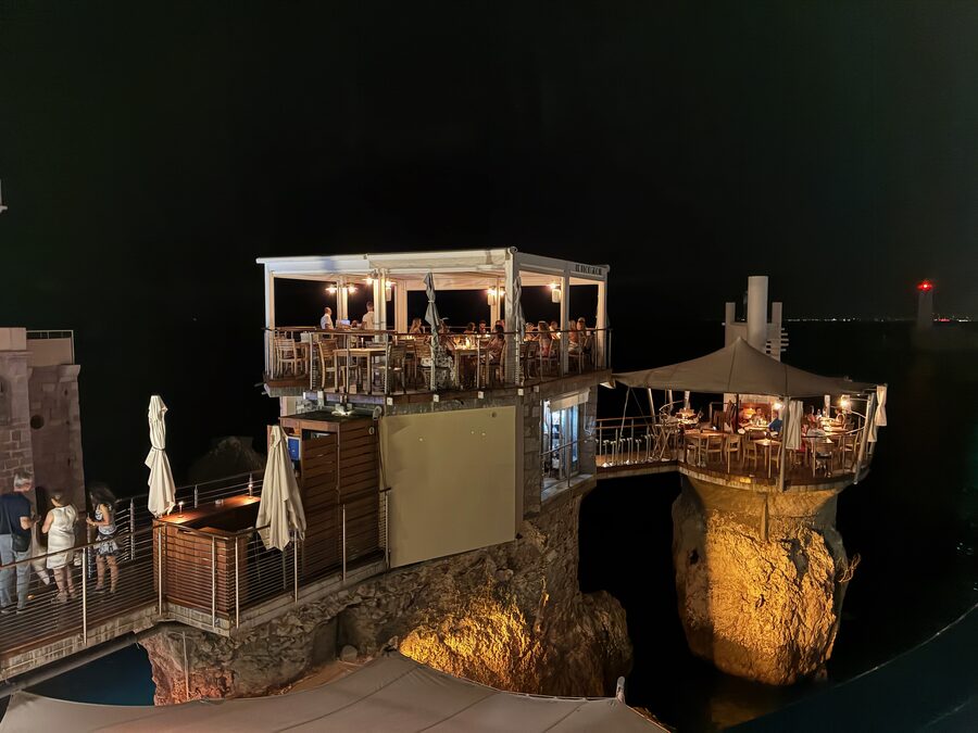 Das Restaurant Le Plongeoir bei Nacht, auf einem beleuchteten Felsen im Meer in Nizza